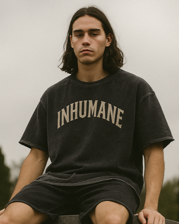 Person wearing a black 'INHUMANE' t-shirt sitting on a gravestone in a cemetery.